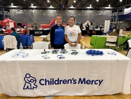 Children's Mercy team attending the Tu Salud health fair; two women standing at a table with a white Children's Mercy tablecloth.