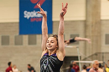 Broken knuckle patient, Ashton, smiling with her arms up at a gymnastics tournament